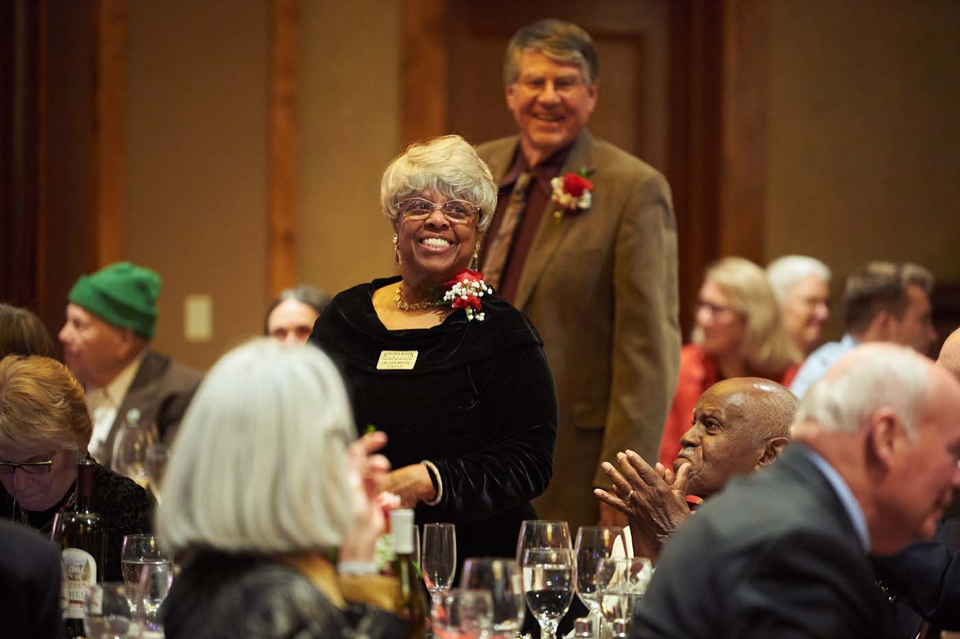 a woman and a man standing in a crowded room while other people clap