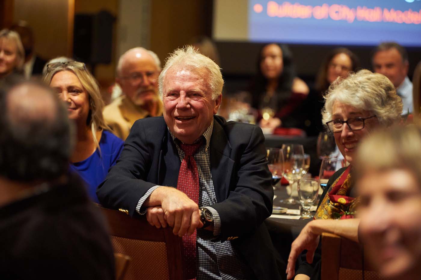 a man sitting in a crowded event room, smiling
