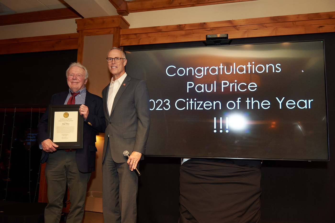 Two people standing on a stage, with one man accepting an award for citizen of the year
