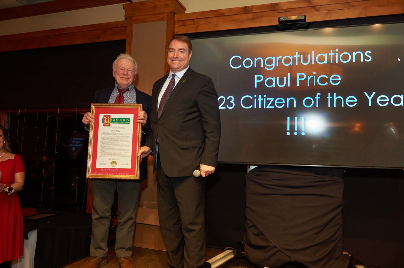 Two people standing on a stage, with one man accepting an award for citizen of the year