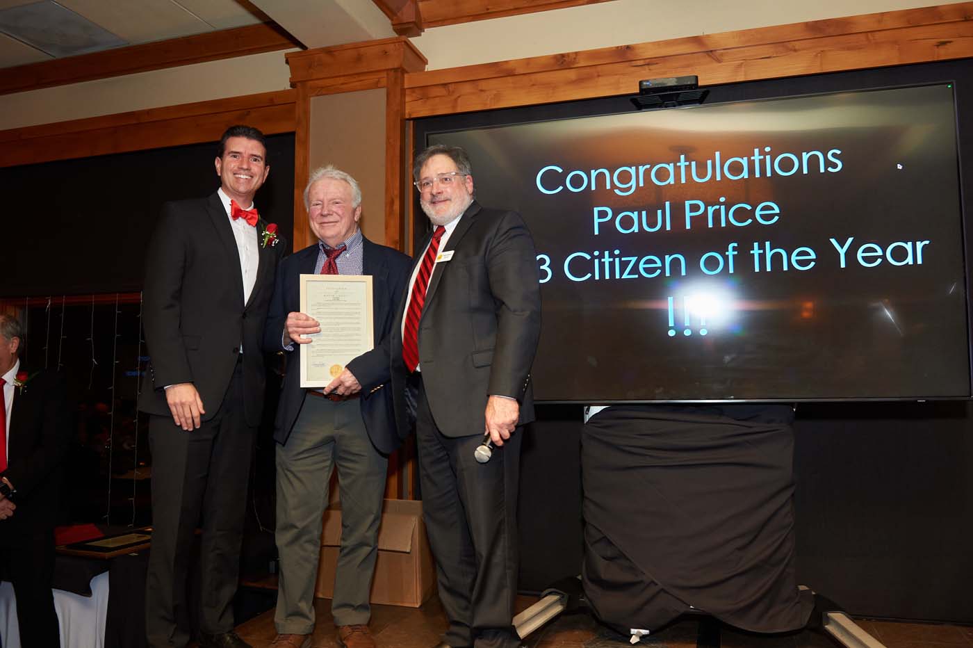 Three people standing on a stage, with one man accepting an award for citizen of the year