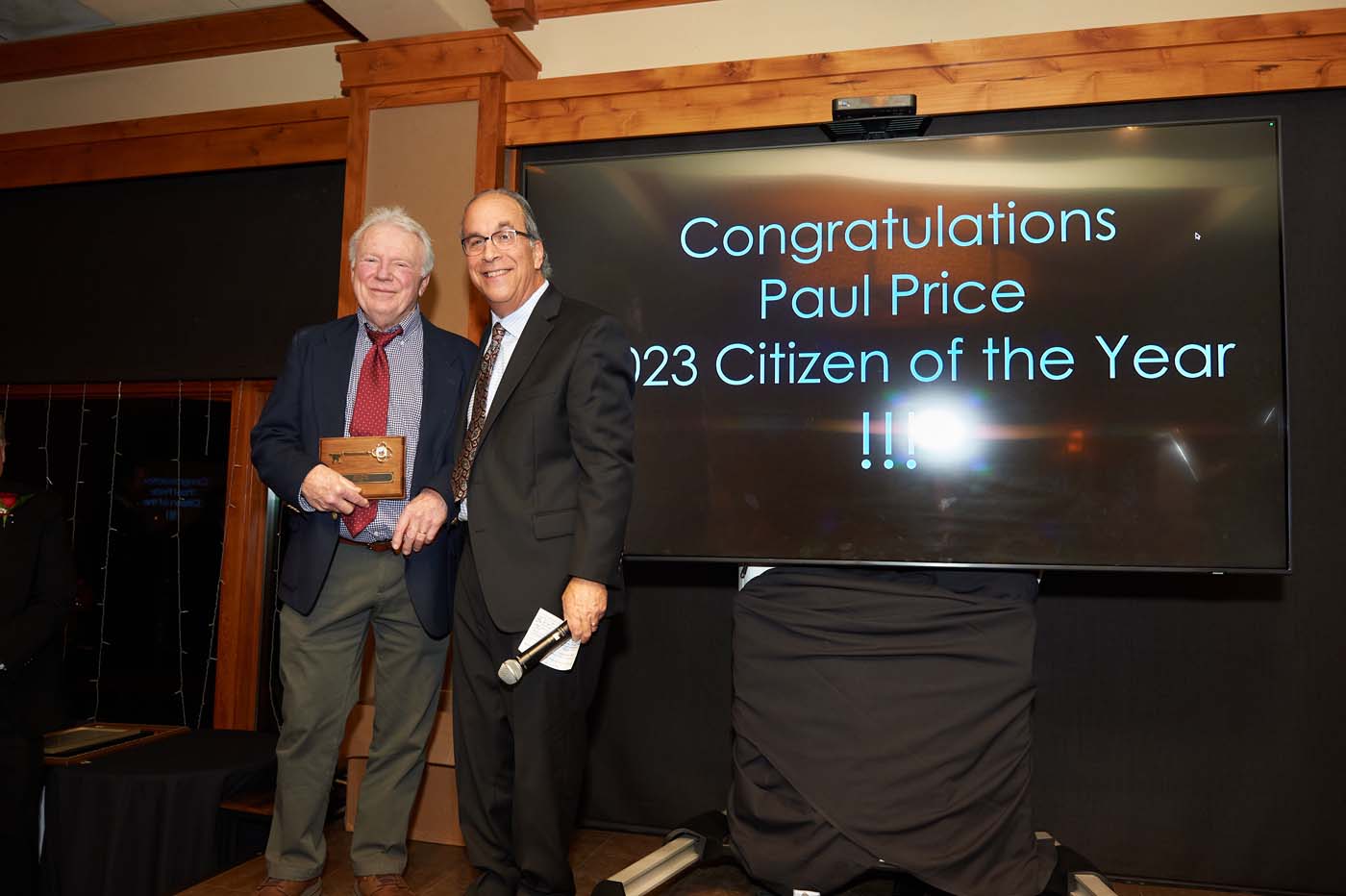 Two people standing on a stage, with one man accepting an award for citizen of the year