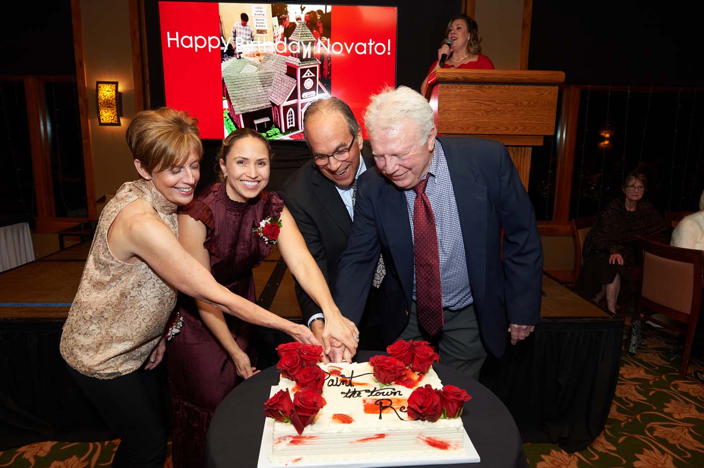 four people posing and cutting a cake