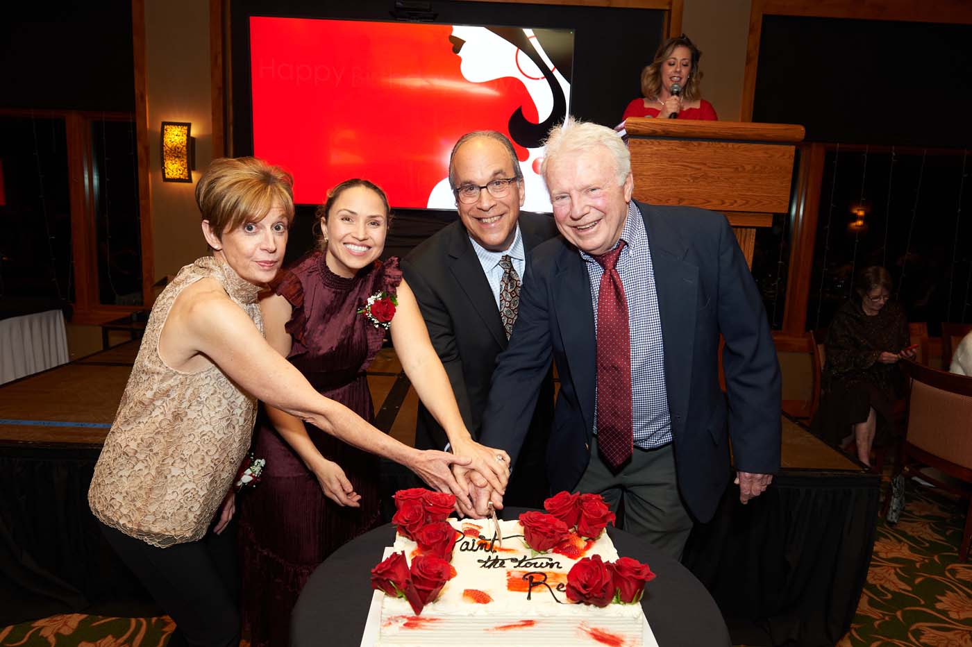 four people posing and cutting a cake